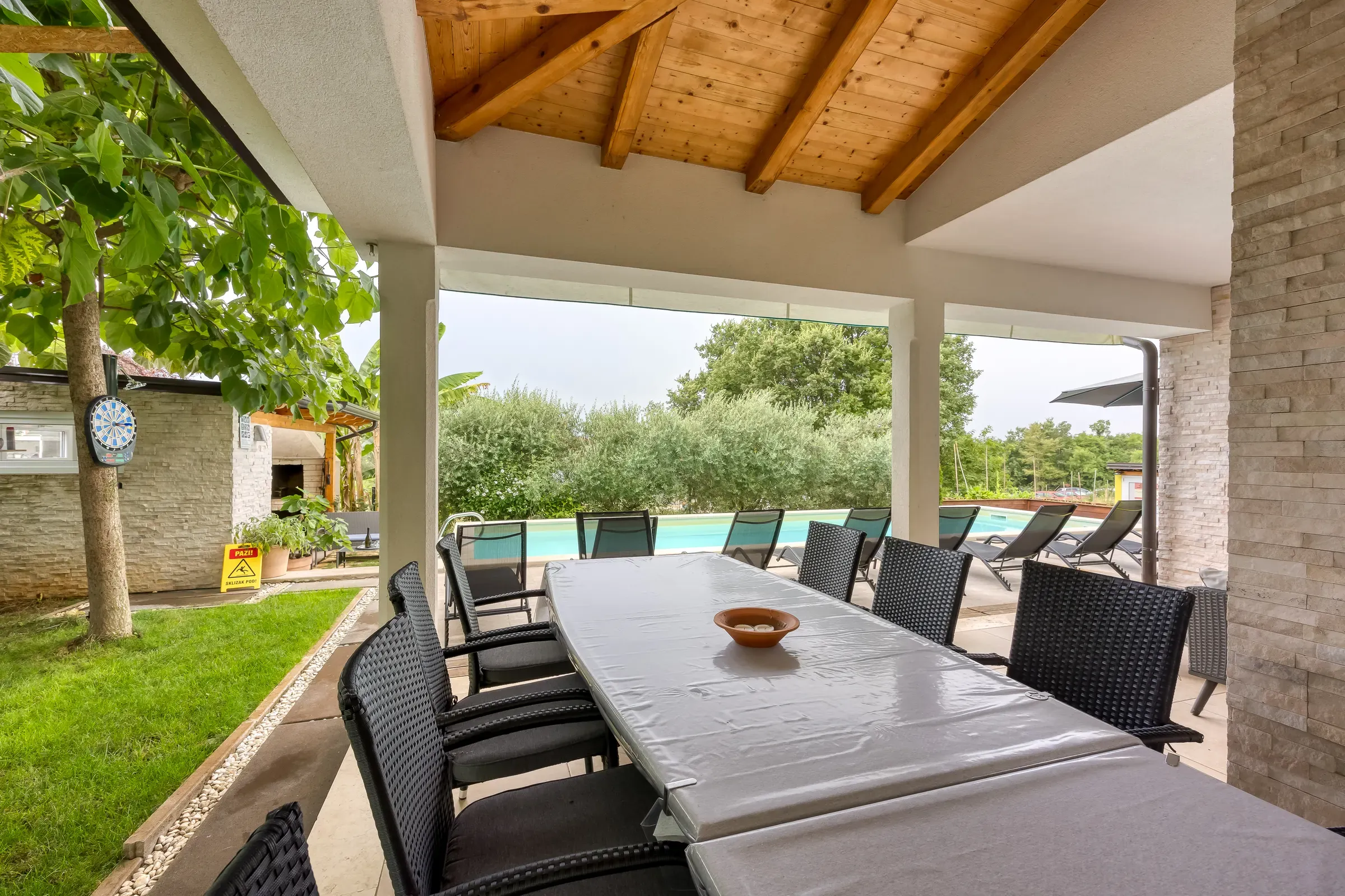 Covered terrace with a long dining table overlooking the pool and garden